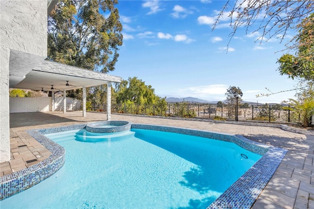 view of swimming pool featuring a fenced backyard, a mountain view, a pool with connected hot tub, a ceiling fan, and a patio area