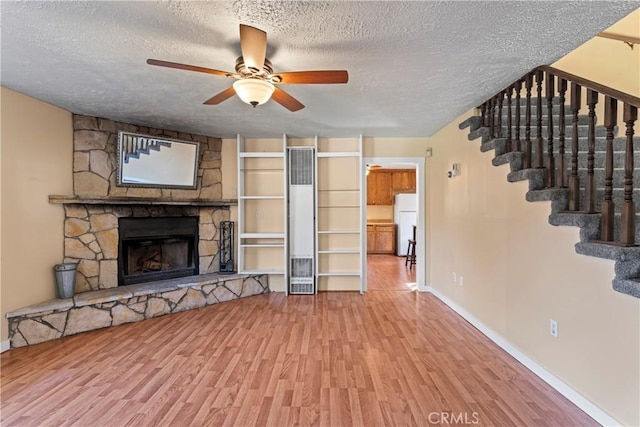 unfurnished living room featuring a fireplace, stairway, a ceiling fan, a textured ceiling, and wood finished floors