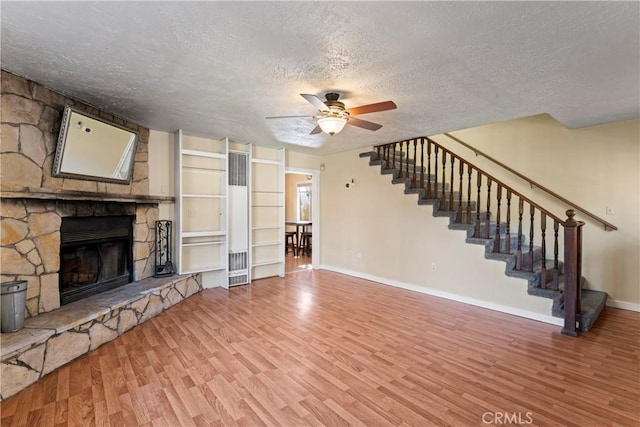 unfurnished living room featuring a textured ceiling, a fireplace, wood finished floors, a ceiling fan, and stairs