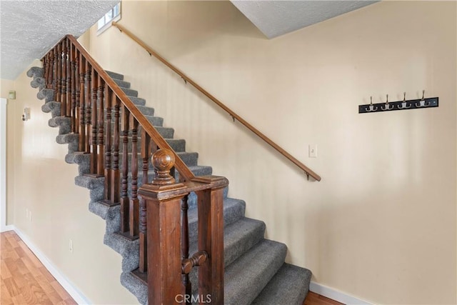 stairs with a textured ceiling, wood finished floors, and baseboards