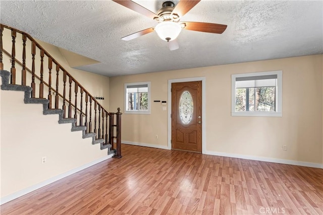 foyer entrance featuring stairs, a textured ceiling, wood finished floors, and baseboards