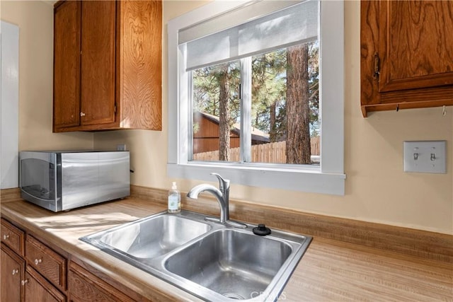 kitchen featuring brown cabinetry, light countertops, stainless steel microwave, and a sink