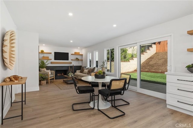 dining area with a warm lit fireplace, light wood-style flooring, and recessed lighting