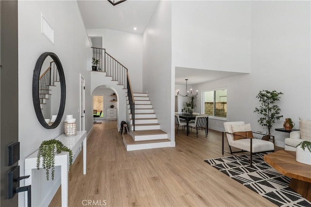 foyer with arched walkways, a notable chandelier, light wood finished floors, visible vents, and stairway