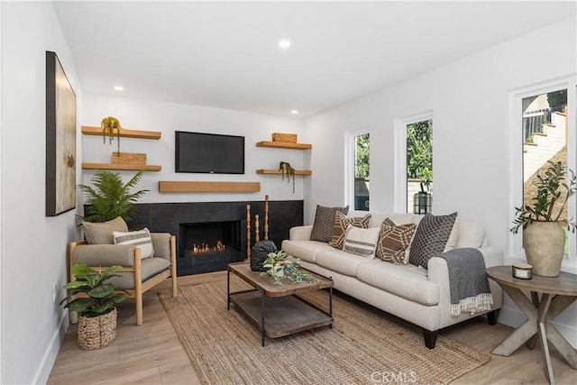 living area featuring light wood finished floors, a lit fireplace, baseboards, and recessed lighting