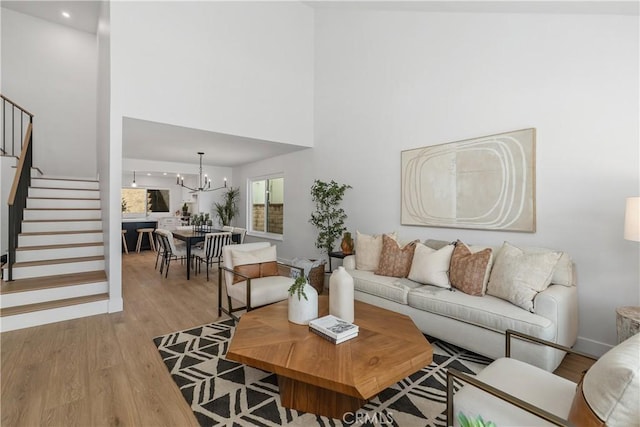 living area featuring stairs, light wood finished floors, a high ceiling, and an inviting chandelier