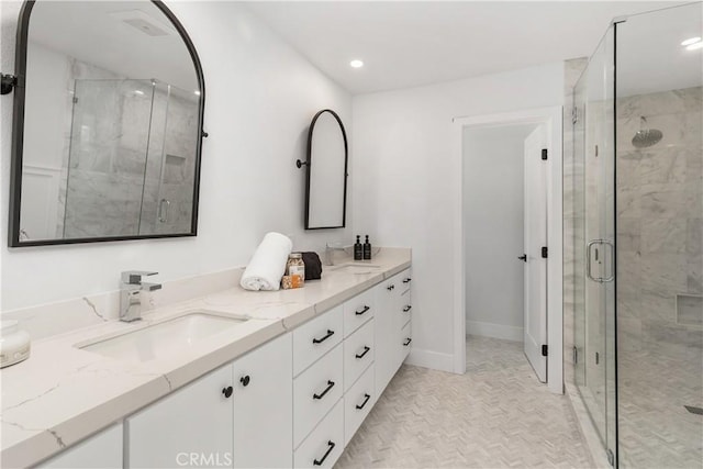 full bath with double vanity, a stall shower, a sink, and baseboards