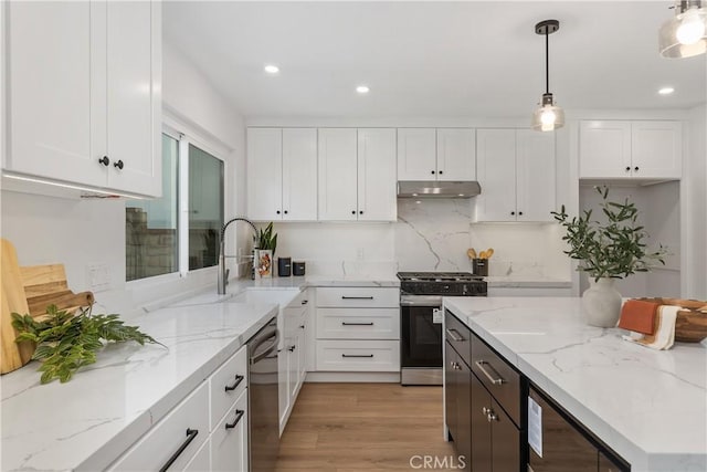 kitchen featuring under cabinet range hood, stainless steel appliances, a sink, white cabinetry, and light stone countertops