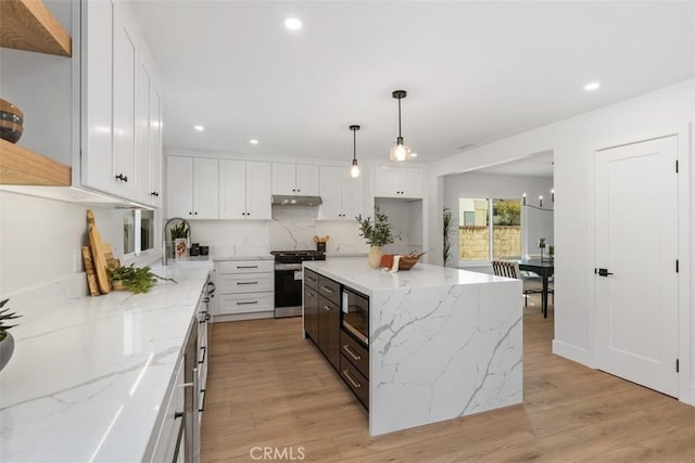 kitchen featuring light wood-style floors, black microwave, under cabinet range hood, and gas range