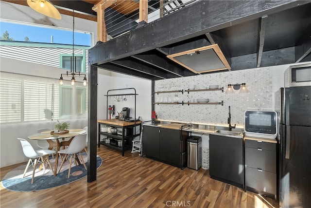 kitchen with dark wood-style floors, stainless steel microwave, backsplash, freestanding refrigerator, and a sink