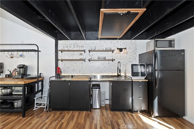 kitchen featuring freestanding refrigerator, stainless steel microwave, a sink, and wood finished floors