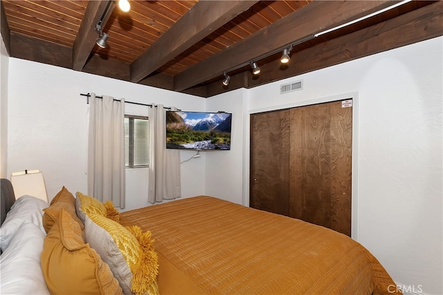 bedroom featuring beamed ceiling, a closet, wood ceiling, and rail lighting