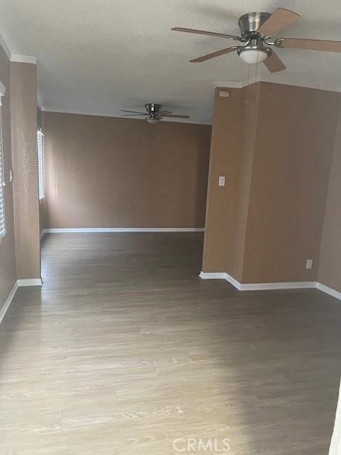 empty room with ceiling fan, light wood-style flooring, baseboards, and a textured ceiling