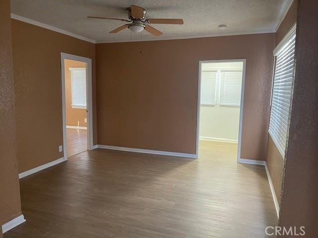 empty room featuring crown molding, a textured ceiling, baseboards, and wood finished floors