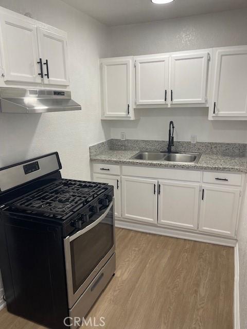 kitchen with under cabinet range hood, stainless steel range with gas cooktop, white cabinets, and a sink