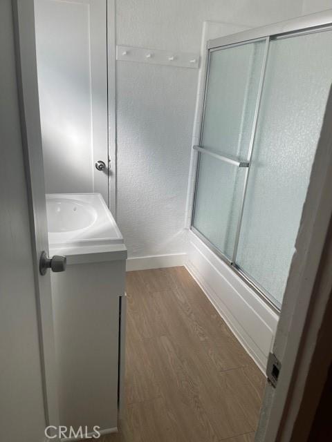 bathroom with vanity, wood finished floors, a shower with shower door, and baseboards