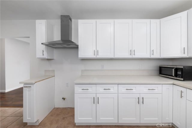 kitchen with wall chimney exhaust hood, stainless steel microwave, and white cabinetry