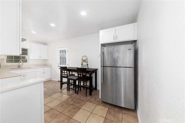 kitchen featuring light tile patterned floors, light countertops, freestanding refrigerator, white cabinets, and a sink