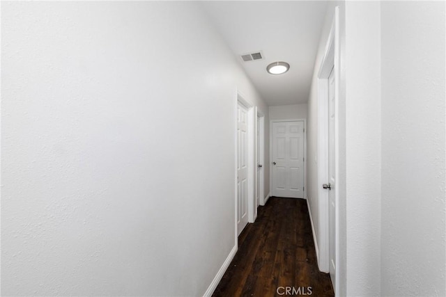 corridor with dark wood-style flooring, visible vents, and baseboards