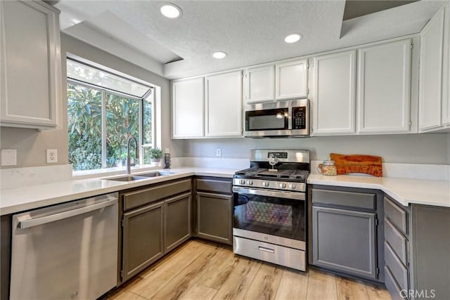 kitchen featuring appliances with stainless steel finishes, light countertops, gray cabinetry, light wood-type flooring, and a sink