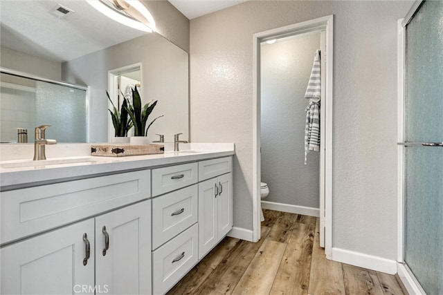 full bath featuring visible vents, toilet, a sink, a shower stall, and wood finished floors