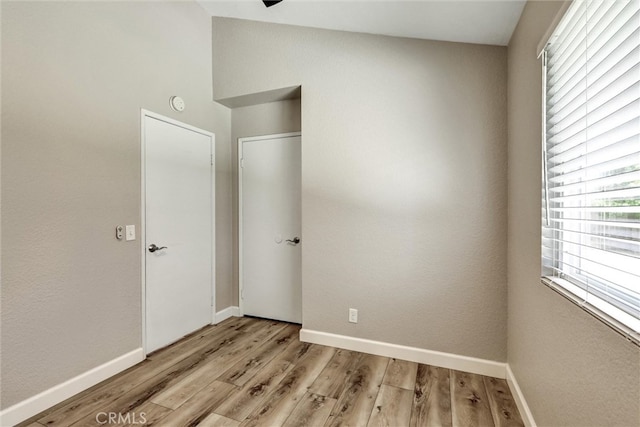 unfurnished bedroom with light wood-style floors, lofted ceiling, and baseboards