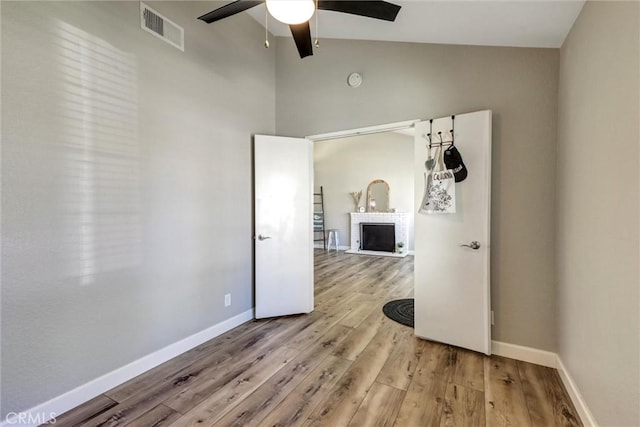 spare room with light wood finished floors, lofted ceiling, visible vents, a brick fireplace, and baseboards