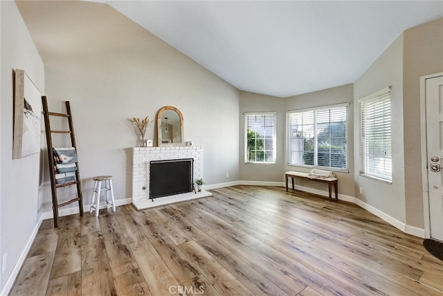 unfurnished living room with lofted ceiling, a fireplace, baseboards, and wood finished floors