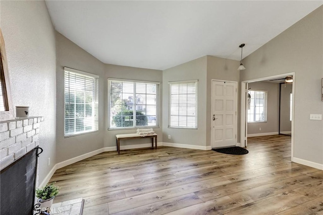 unfurnished living room featuring lofted ceiling, a fireplace, baseboards, and wood finished floors