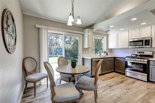 kitchen with light countertops, hanging light fixtures, light wood-style flooring, appliances with stainless steel finishes, and white cabinets