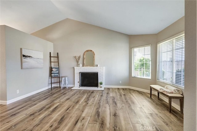 living room with light wood-style flooring, a fireplace, baseboards, and vaulted ceiling