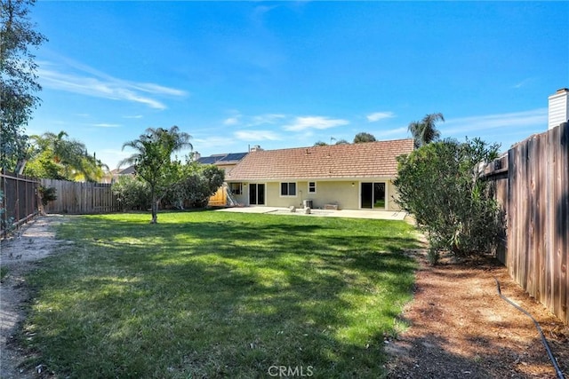 rear view of house with solar panels, a fenced backyard, a lawn, and a patio