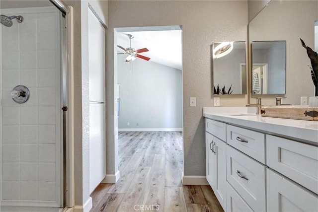 bathroom with double vanity, a ceiling fan, a sink, wood finished floors, and tiled shower