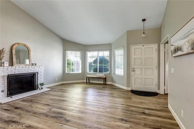 foyer entrance with a fireplace, vaulted ceiling, baseboards, and wood finished floors