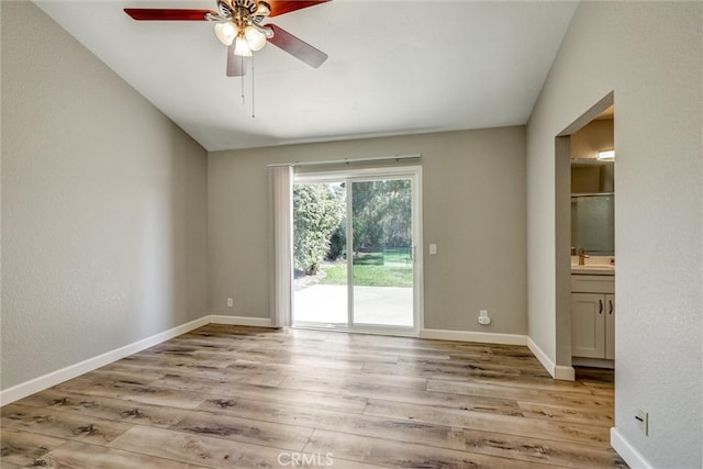 spare room with vaulted ceiling, light wood-type flooring, a ceiling fan, and baseboards