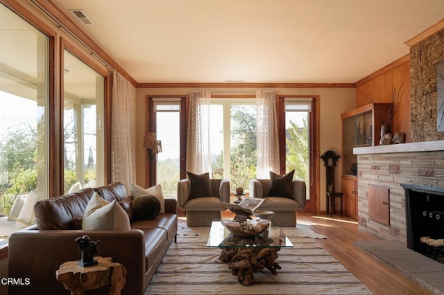 living room featuring crown molding, visible vents, wood finished floors, and a stone fireplace