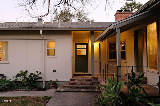 view of exterior entry featuring roof with shingles and a chimney