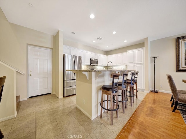 kitchen featuring white cabinetry, light stone countertops, visible vents, and appliances with stainless steel finishes