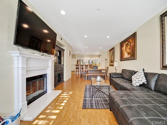 living area featuring light wood finished floors, recessed lighting, and a glass covered fireplace