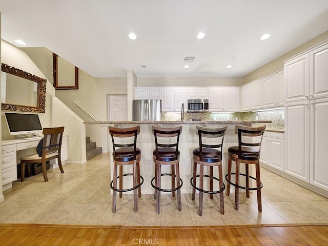 kitchen with stainless steel appliances, backsplash, light stone countertops, and white cabinets