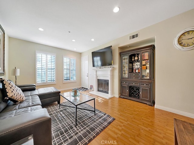 living area with recessed lighting, visible vents, light wood-style floors, a glass covered fireplace, and baseboards