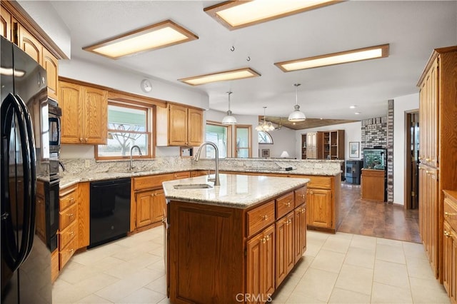 kitchen with black appliances, a peninsula, a center island with sink, and a sink