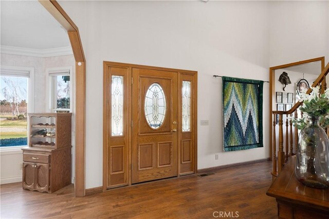 foyer entrance with visible vents, ornamental molding, baseboards, and wood finished floors