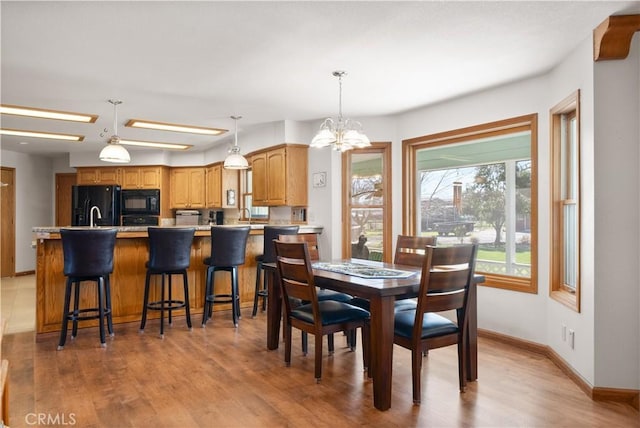 dining area featuring baseboards, light wood finished floors, and a chandelier