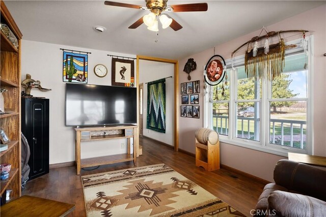 living area featuring a wealth of natural light, baseboards, ceiling fan, and wood finished floors