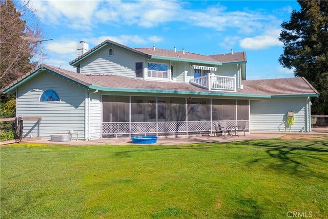 rear view of property featuring a lawn, a sunroom, a balcony, a chimney, and a patio area