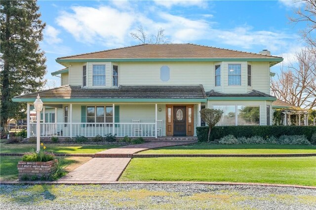 country-style home with covered porch, a chimney, and a front lawn