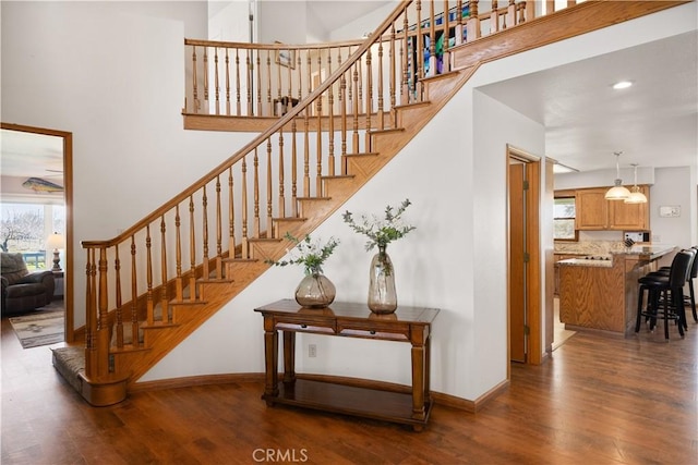 staircase featuring recessed lighting, a high ceiling, baseboards, and wood finished floors