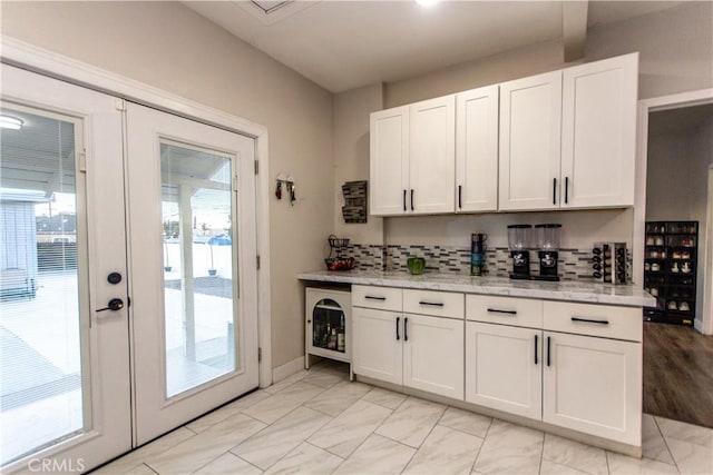 kitchen with light stone counters, french doors, white cabinetry, and decorative backsplash