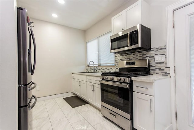 kitchen featuring stainless steel appliances, a sink, white cabinets, light countertops, and decorative backsplash